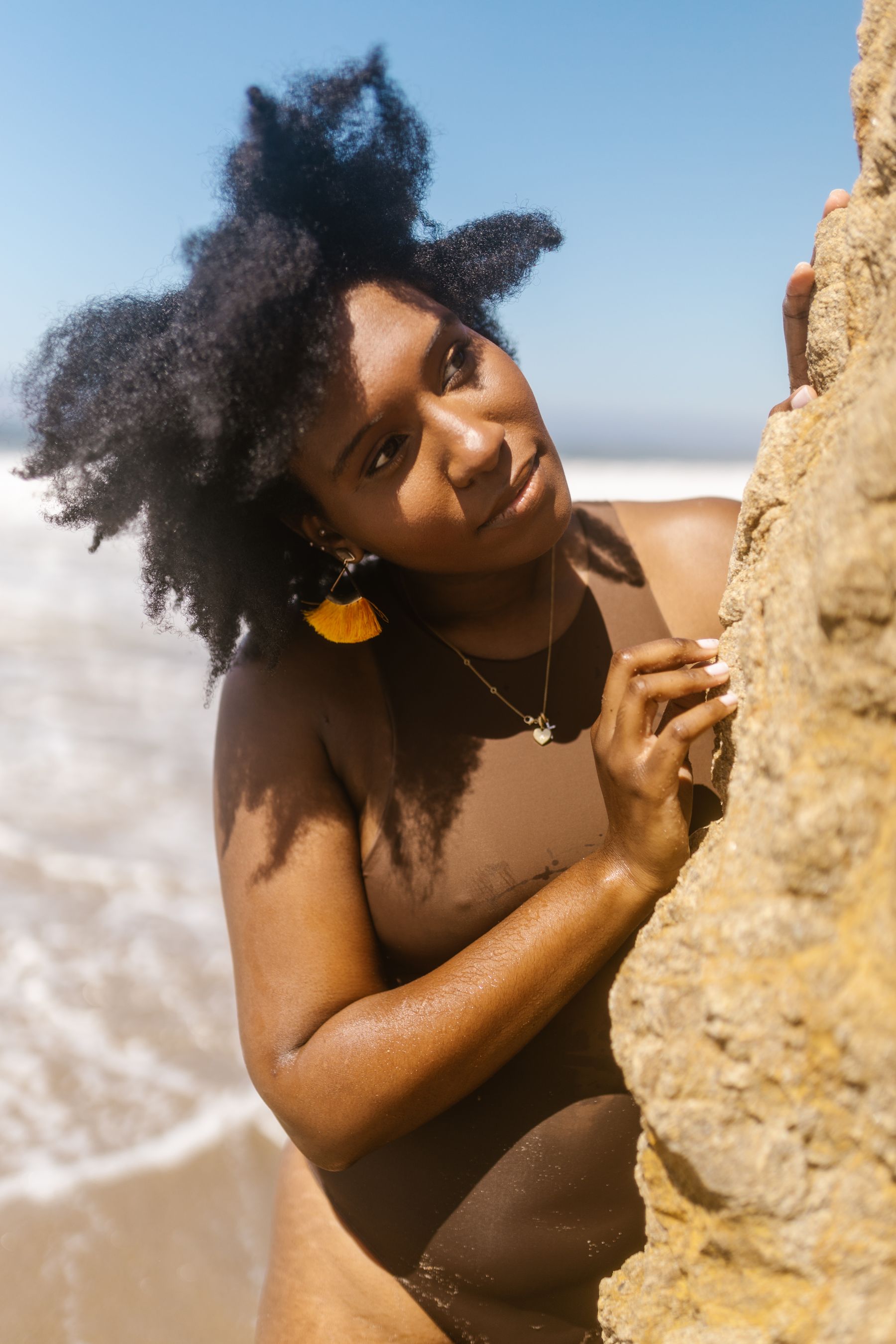 Woman in a brown swimsuit beside a sunlit beach rock